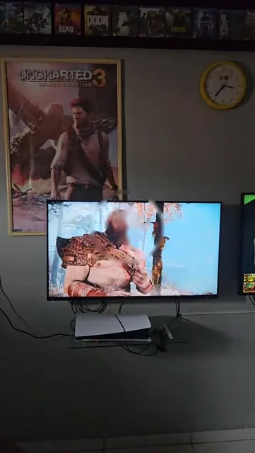PS5 ligado na TV com pôster de Uncharted 3 na parede